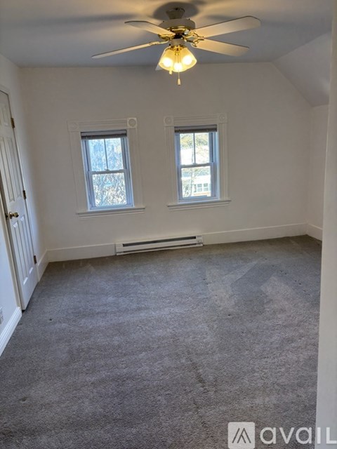 A room with a carpeted floor, a ceiling fan, and two windows.