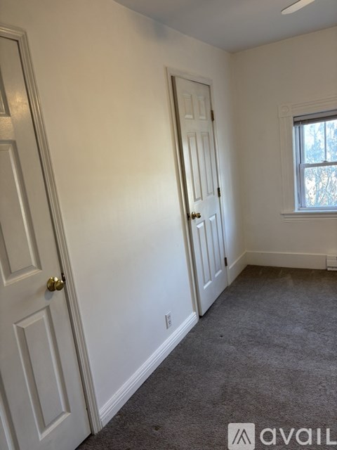 A room with a carpeted floor, a white door, and a window with a view of trees outside.
