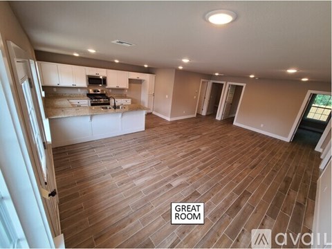 A spacious room with wooden flooring and a kitchen area in the background.