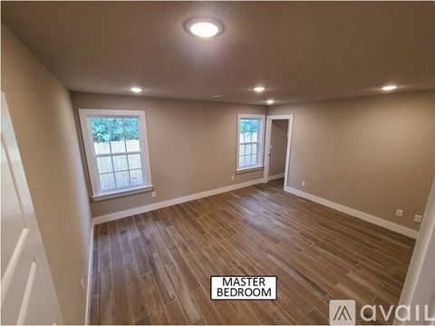 A master bedroom with hardwood floors and two windows.