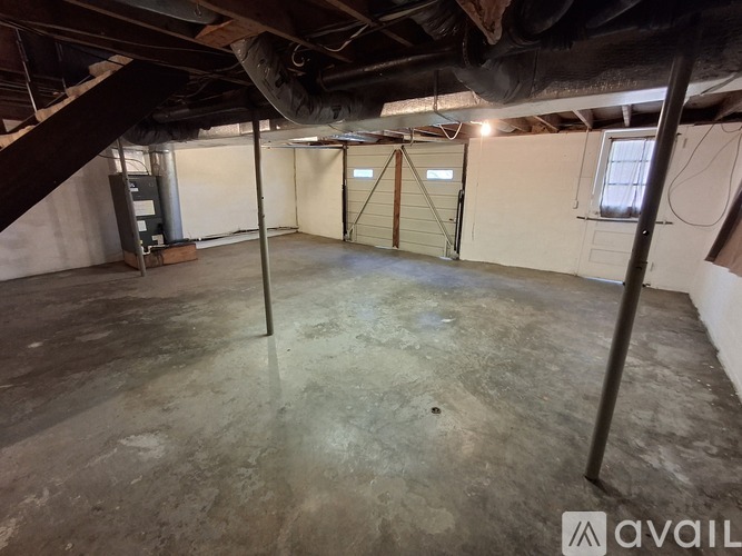 A spacious basement with a concrete floor and walls, featuring a garage door and a door with a window.