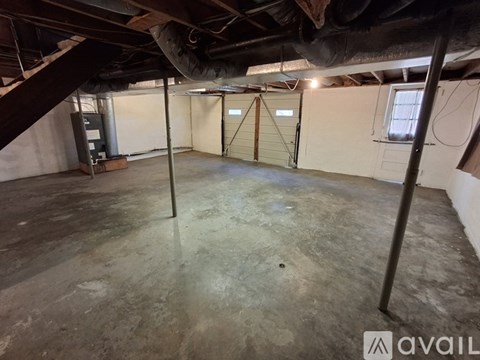 A spacious basement with a concrete floor and walls, featuring a garage door and a door with a window.