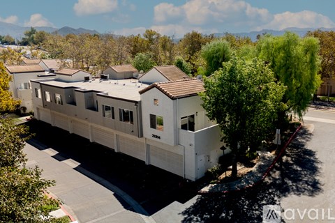 A modern house with a flat roof and a garage is surrounded by trees and has a mountain in the background.