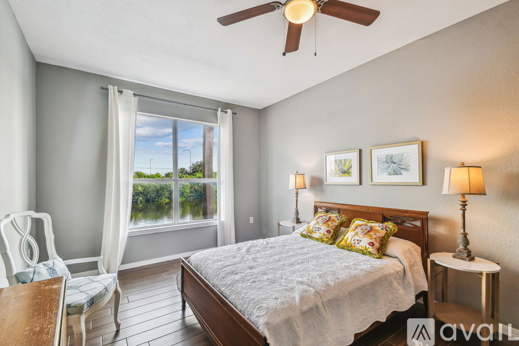 A bedroom with a large bed, a ceiling fan, and a view of the outdoors through a window.