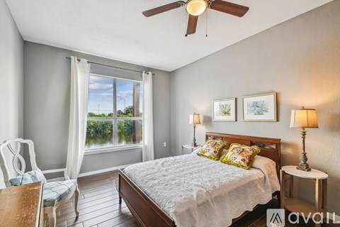 A bedroom with a large bed, a ceiling fan, and a view of the outdoors through a window.