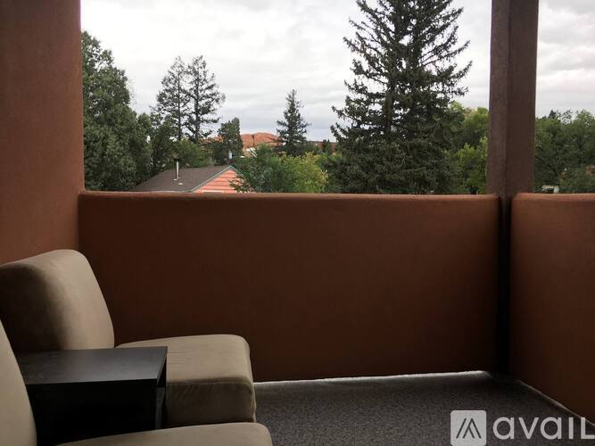 A room with a chair and a table with a view of trees and a house.