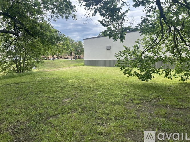A grassy field with a building in the background and trees in the foreground.