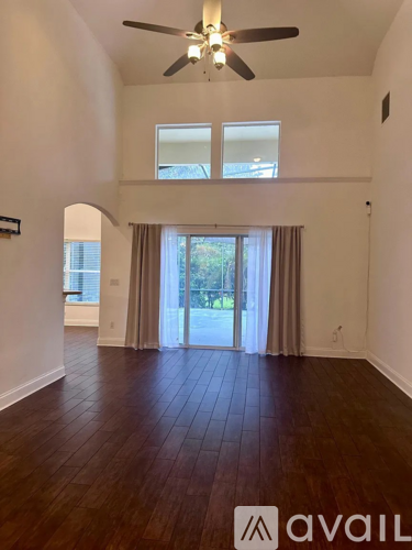 A spacious room with a ceiling fan and hardwood flooring.