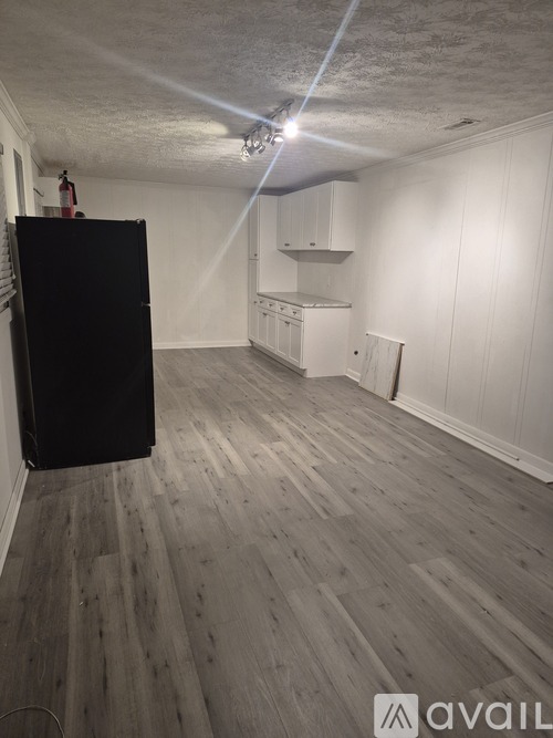 A room with a black refrigerator and wooden flooring.