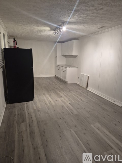 A room with a black refrigerator and wooden flooring.