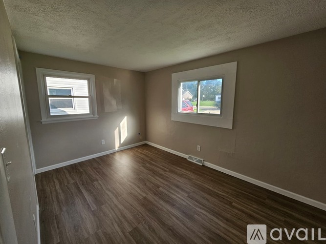 A room with wooden flooring and two windows.