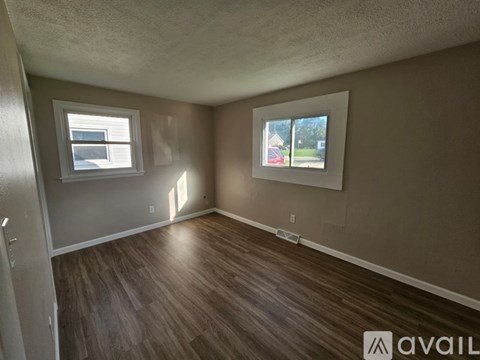 A room with wooden flooring and two windows.