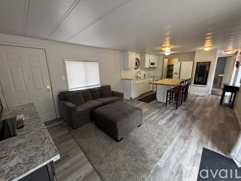 A living room with a grey couch and a kitchen area in the background.