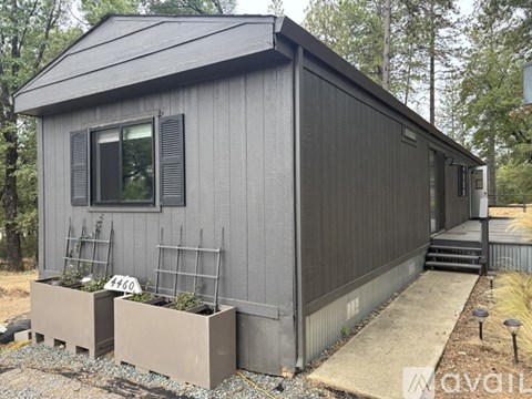 A grey house with a black roof and a window with black shutters.