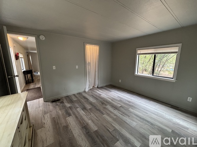 A room with wooden flooring and a window with a view of trees.