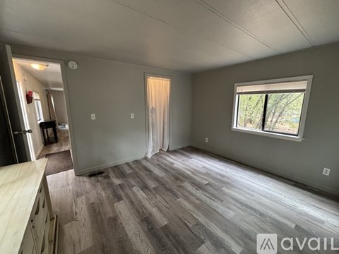A room with wooden flooring and a window with a view of trees.