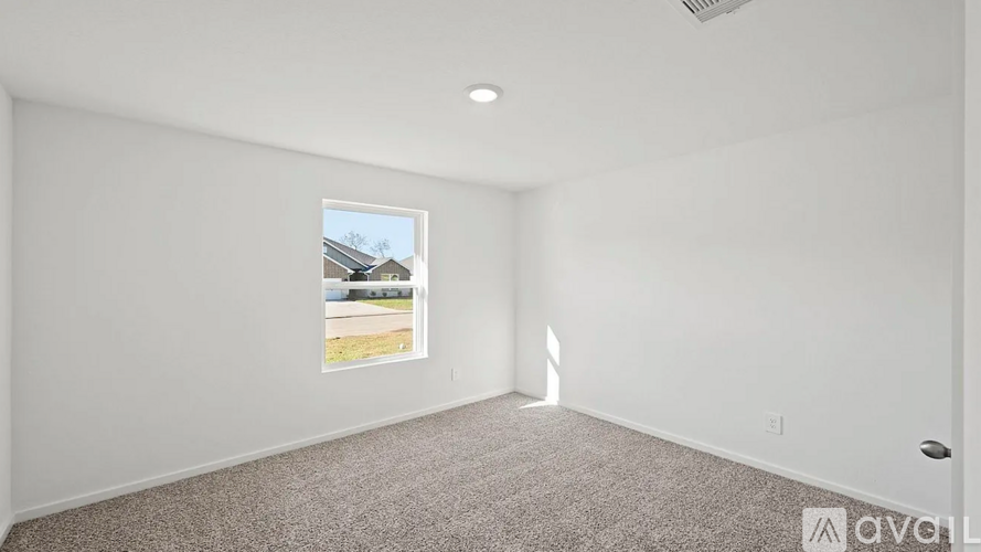 A room with a carpeted floor and a window showing a residential area outside.