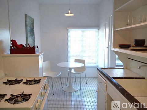 A kitchen with a white stove top oven and a white table with a white chair.