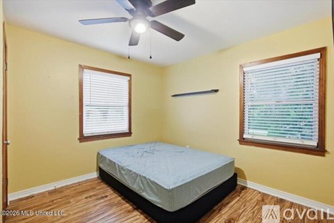 A bedroom with a bed, a ceiling fan, and two windows.