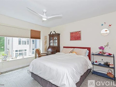 A bedroom with a large bed, a window with blinds, and a ceiling fan.