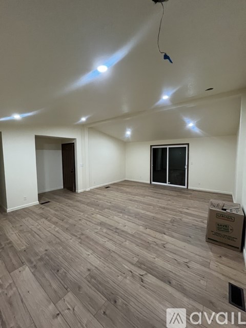 A room with wooden flooring and a box labeled "AVAILABLE" on the floor.