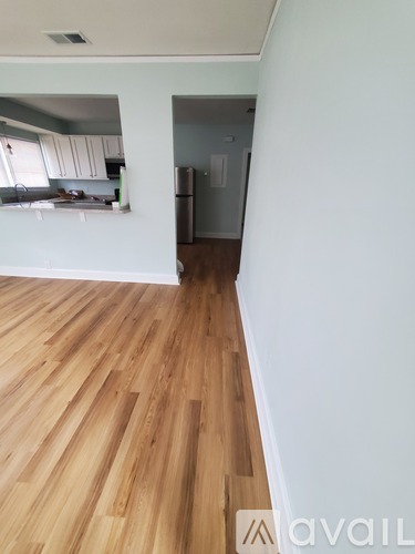 A room with wooden flooring and a kitchen area in the background.
