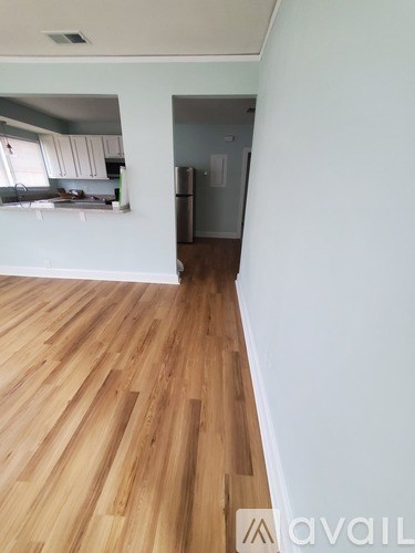 A room with wooden flooring and a kitchen area in the background.