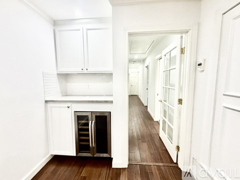 A long hallway with white doors and a kitchen area with a refrigerator and cabinets.