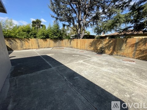 A concrete area with a wooden fence and trees in the background.