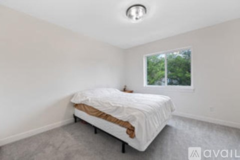 A bedroom with a white bed and a window showing greenery outside.