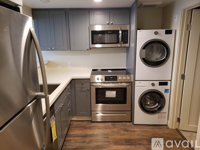 A kitchen with a stainless steel refrigerator, microwave, oven, and washing machine.