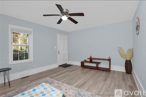 A room with a ceiling fan, a window, a door, a bench, a table, and a vase on the floor.