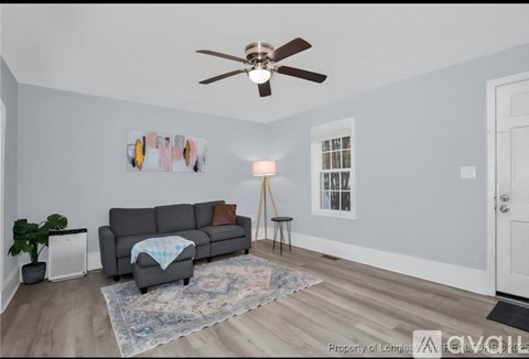 A living room with a grey couch, a rug, a floor lamp, and a ceiling fan.
