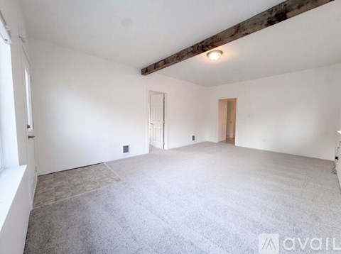 A spacious room with a carpeted floor and a wooden beam on the ceiling.