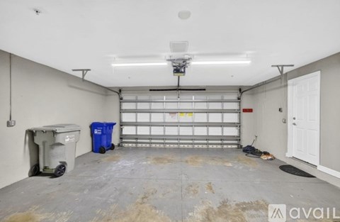 A spacious garage with a white ceiling, a blue bin, and a white door.