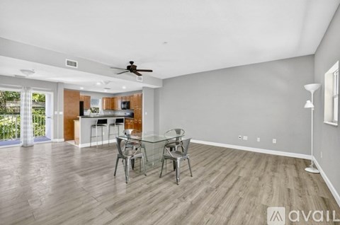 A spacious room with a glass table and chairs, a ceiling fan, and a view of a kitchen area.