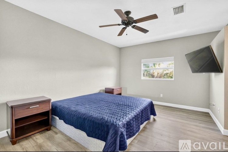 A bedroom with a bed, a ceiling fan, and a window with a view of trees.