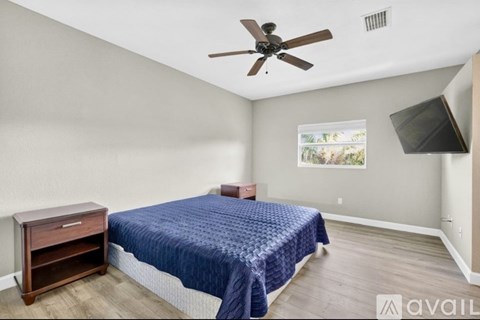 A bedroom with a bed, a ceiling fan, and a window with a view of trees.