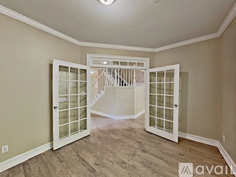 A room with a white door and a staircase in the background.