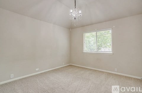 A room with a carpeted floor, a window with blinds, and a chandelier hanging from the ceiling.