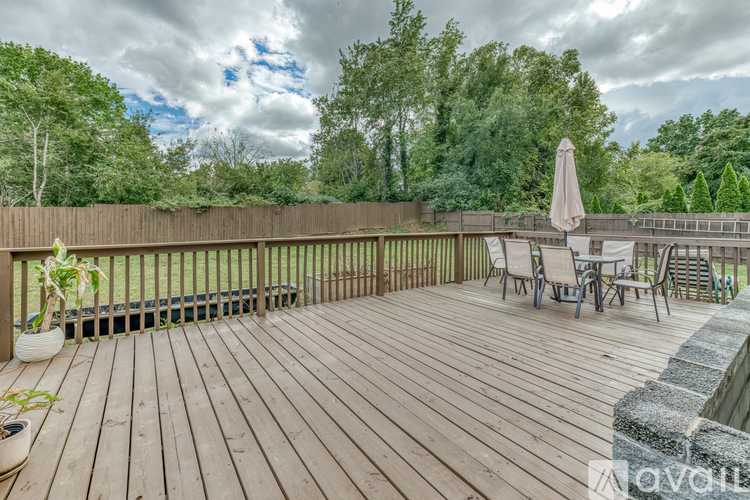 A wooden deck with chairs and an umbrella is surrounded by trees.