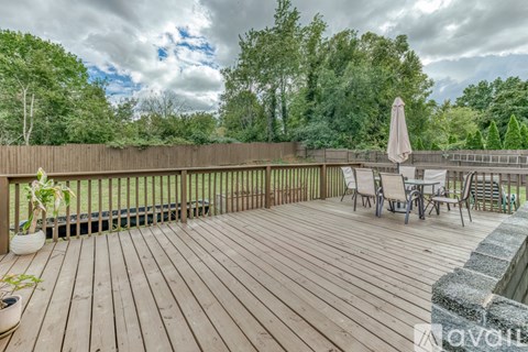 A wooden deck with chairs and an umbrella is surrounded by trees.