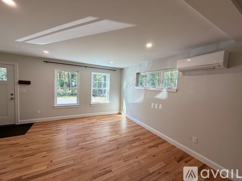 A spacious room with wooden flooring and two windows.