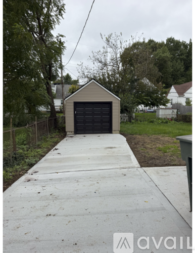 A small building with a black door is situated on a concrete path.