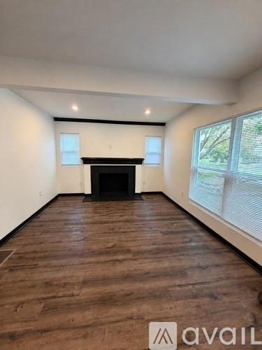A spacious room with wooden flooring and a black fireplace.