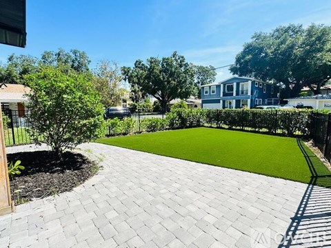 A backyard with a brick walkway and a green lawn.