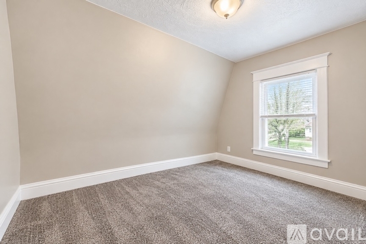 A room with a carpeted floor and a window showing a view of trees and a house.