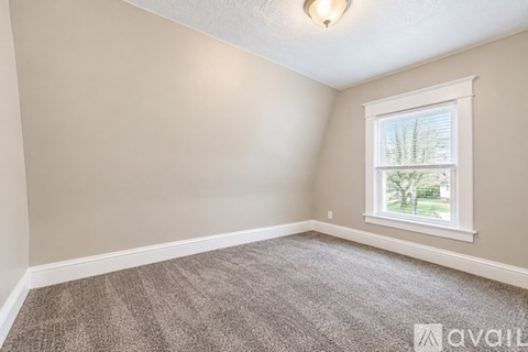A room with a carpeted floor and a window showing a view of trees and a house.