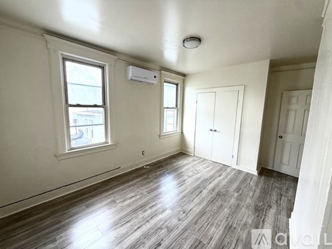 A spacious room with wood flooring and two windows.