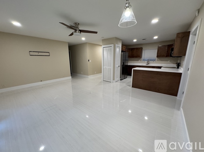 A spacious kitchen and living room with white flooring and a ceiling fan.